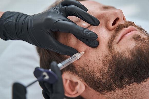 Man with dermal filler needle near cheek 